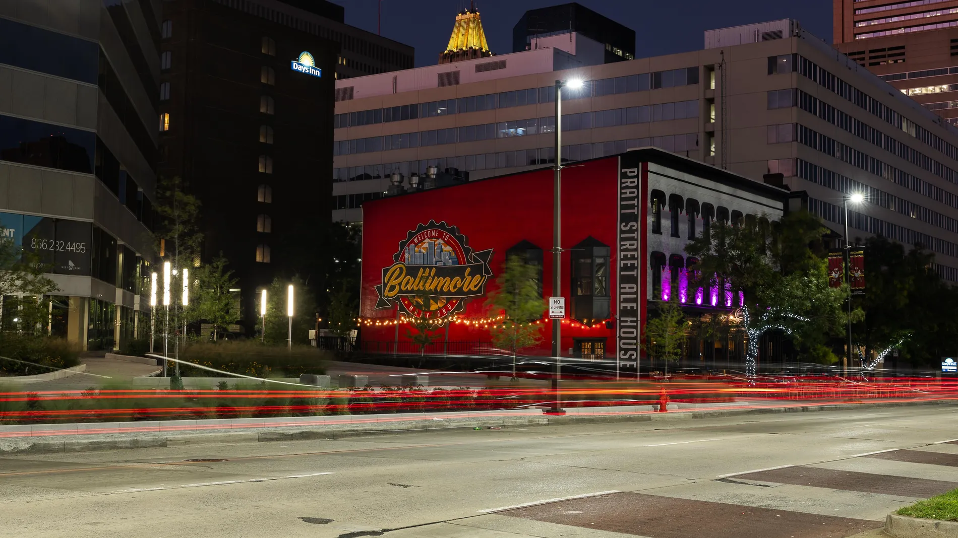 The Pratt Street Ale House mural lit up at night with traffic passing on Pratt Street